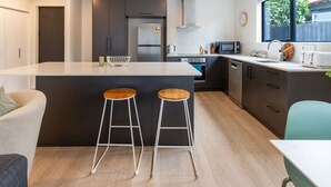 A modern kitchen with a central island, two stools, a microwave, and a sink.