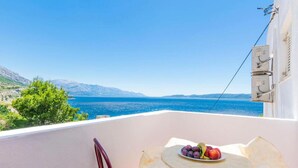 A balcony with a table set with fruit, overlooking a clear blue sea and distant mountains. - Cozy apartment in Omis with lake view (Omis)