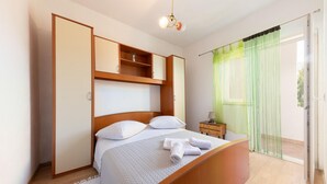A bedroom with a bed, a nightstand, a wardrobe, and a window with sheer curtains. - Cozy apartment in Omis with lake view (Omis)