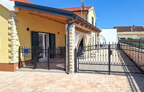 Un edificio amarillo de fachada de piedra, una verja de metal negro y un patio con baldosas.