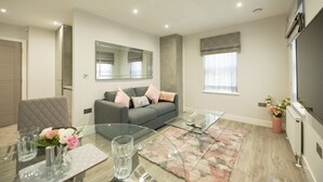 A modern living room with a grey sofa, a glass coffee table, and a dining area with a glass table and chairs. - Chester House (Reading)