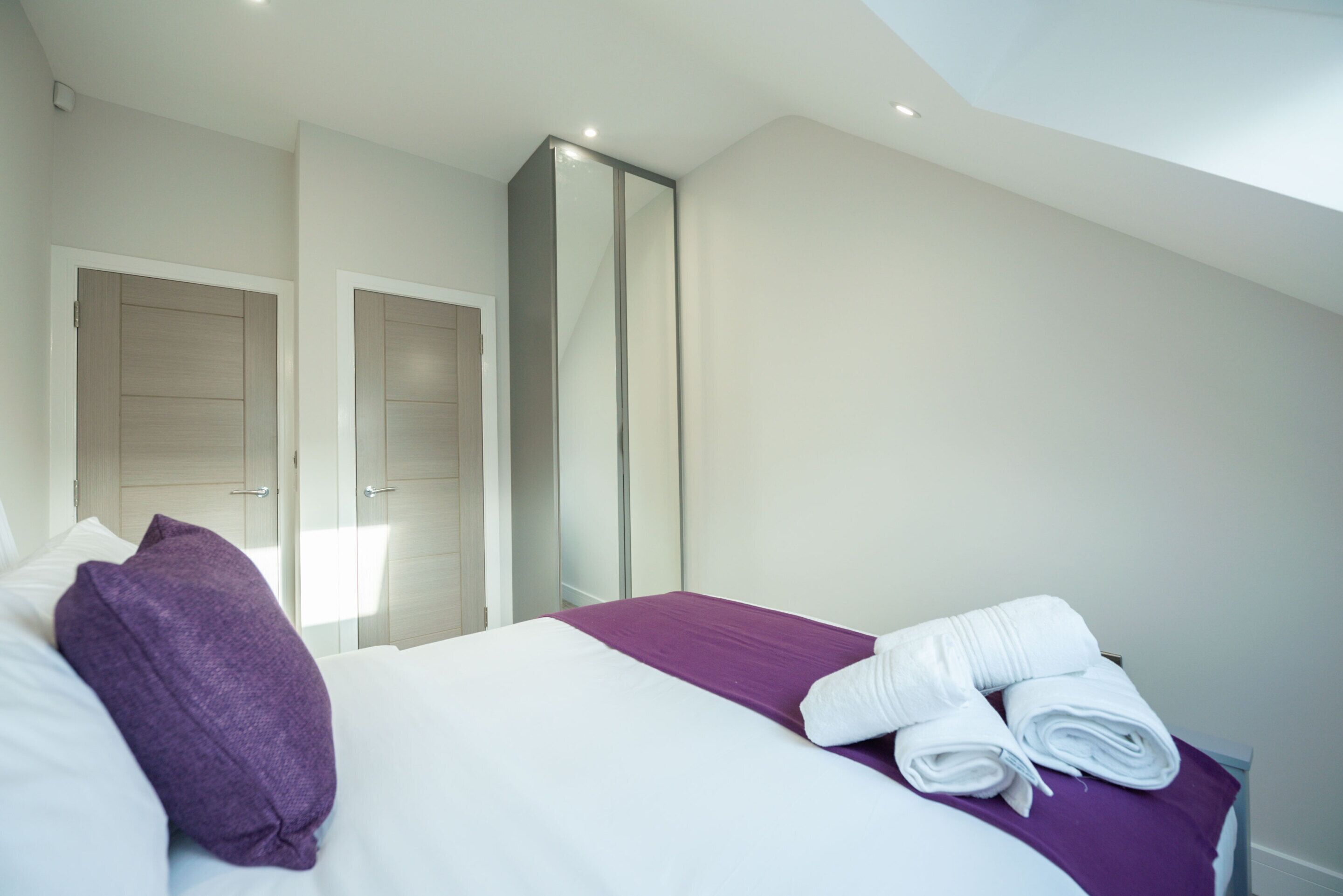 Una habitació d'hotel amb un llit, un coixí morat i tovalloles arremolinades damunt del llit.