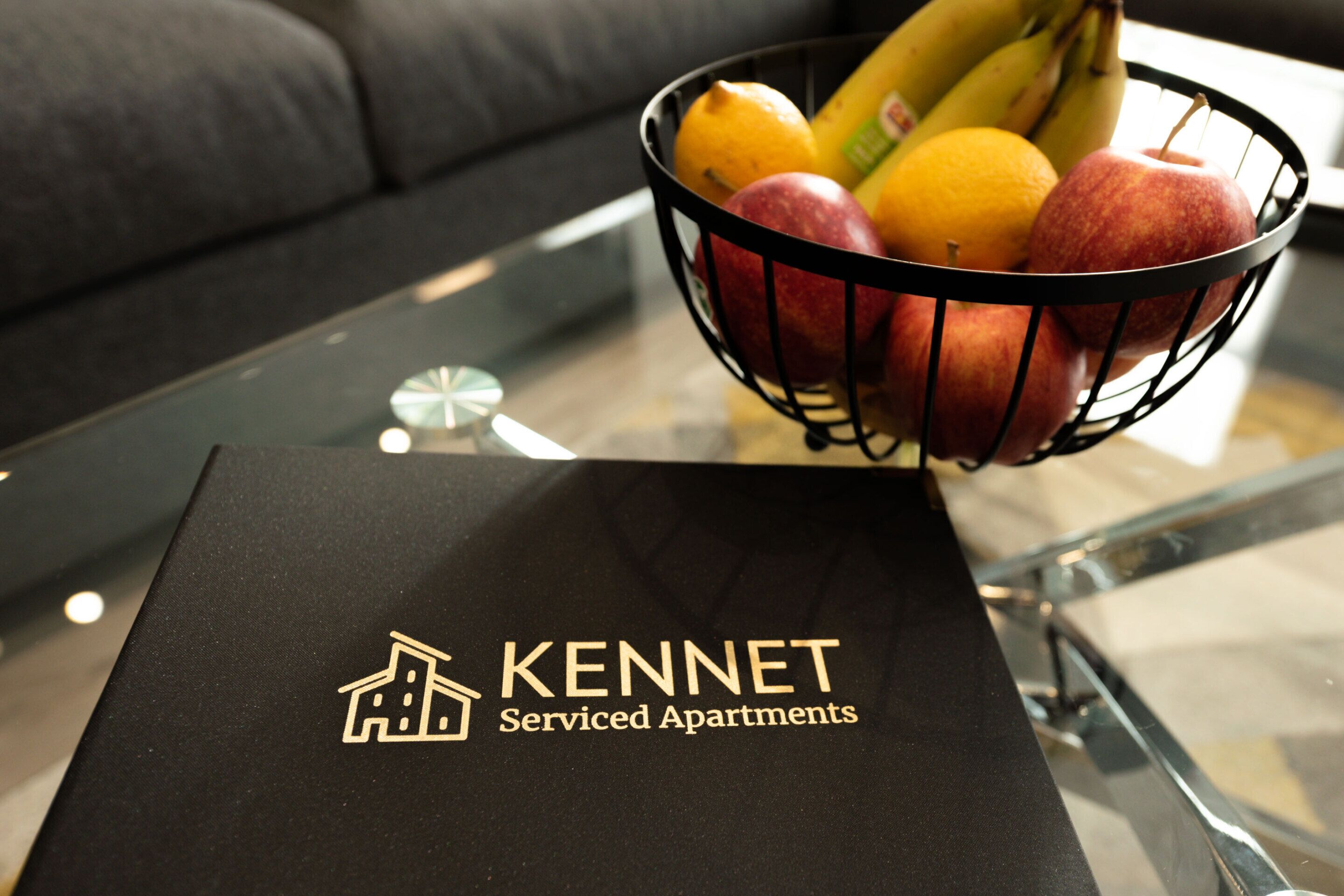 Een zwarte doos met het logo en de naam 'KENNET Serviced Apartments' op een glazen tafel.