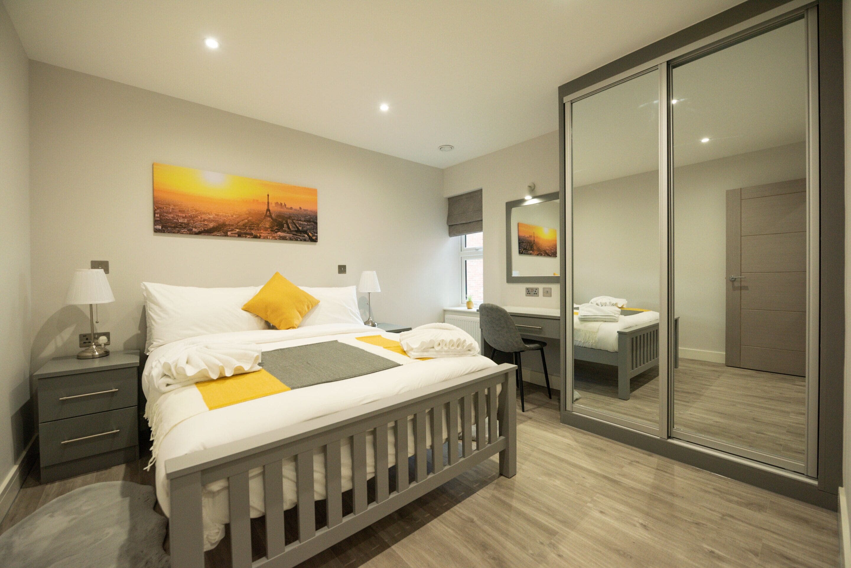 Un dormitorio moderno con cama, mesitas de noche, escritorio y un espejo grande.
