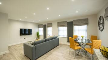 Una sala de estar moderna con un sofá gris, sillas amarillas, una mesa de comedor y un televisor de pantalla plana montado en la pared.