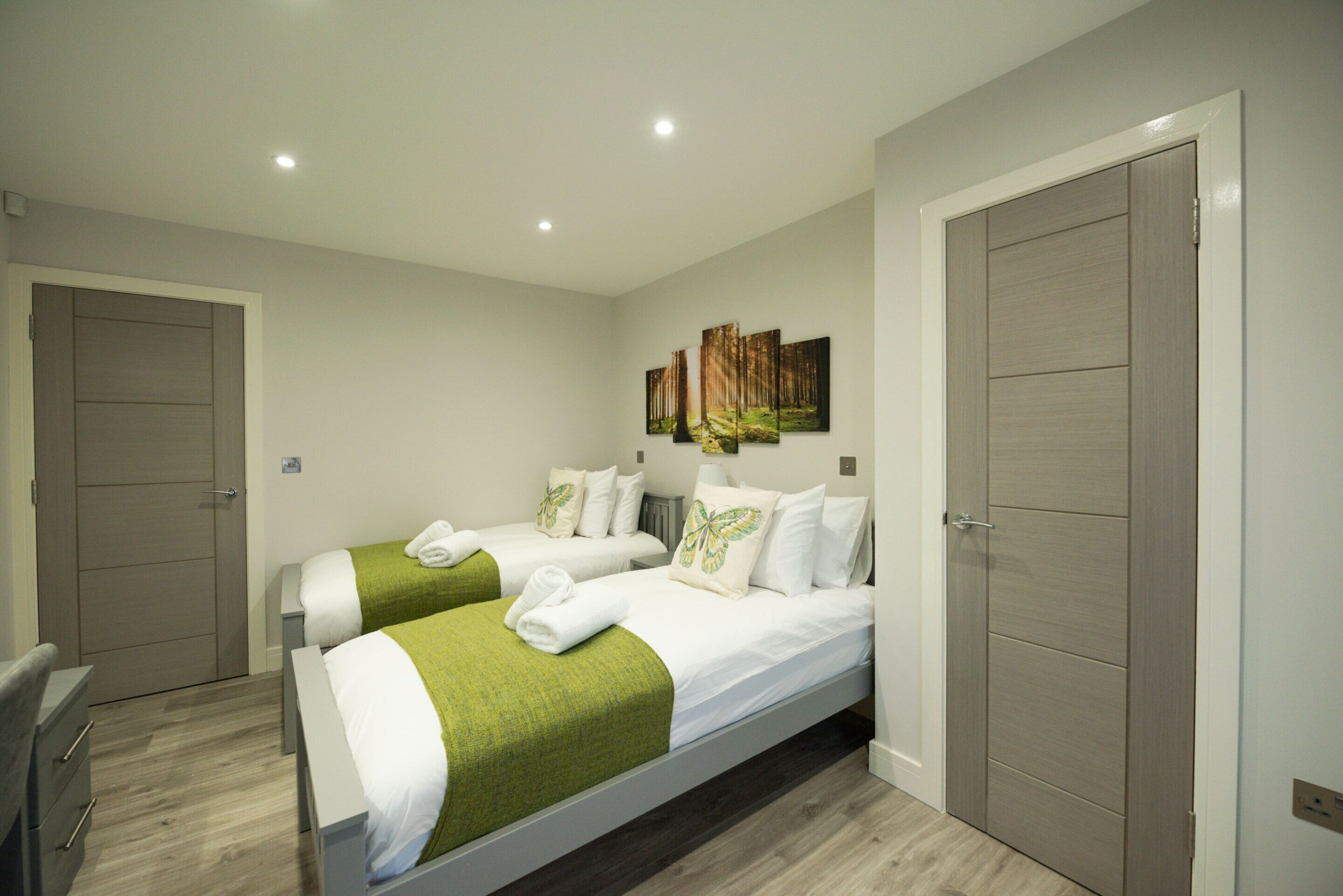 A modern hotel room with two single beds, a wardrobe, and a painting on the wall.