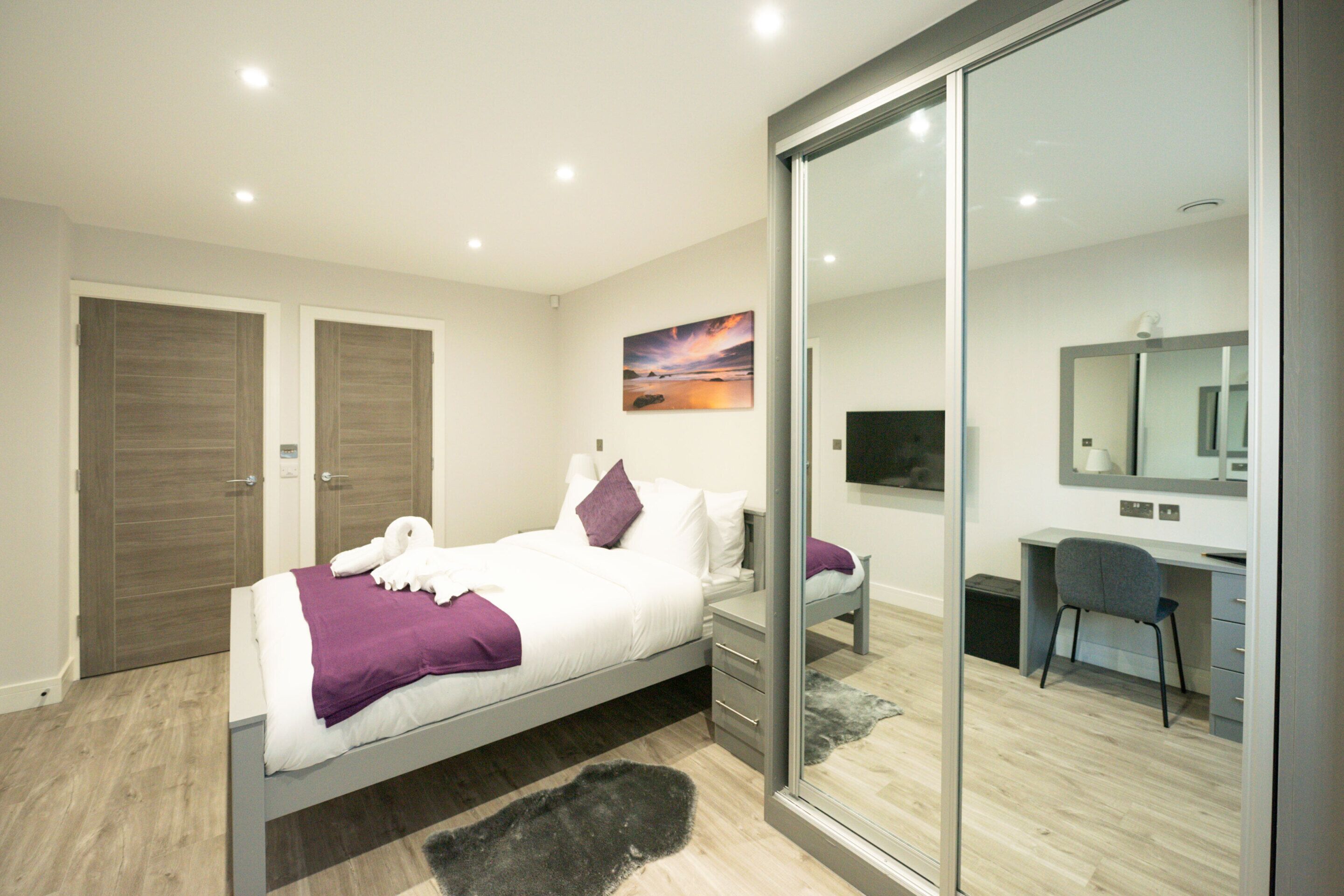 A modern bedroom with a bed, a desk, and a large mirror.