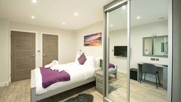 A modern bedroom with a bed, a desk, and a large mirror.