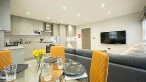 A modern kitchen with built-in appliances, a dining area with a glass table, and a grey sofa. - Chester House (Reading)