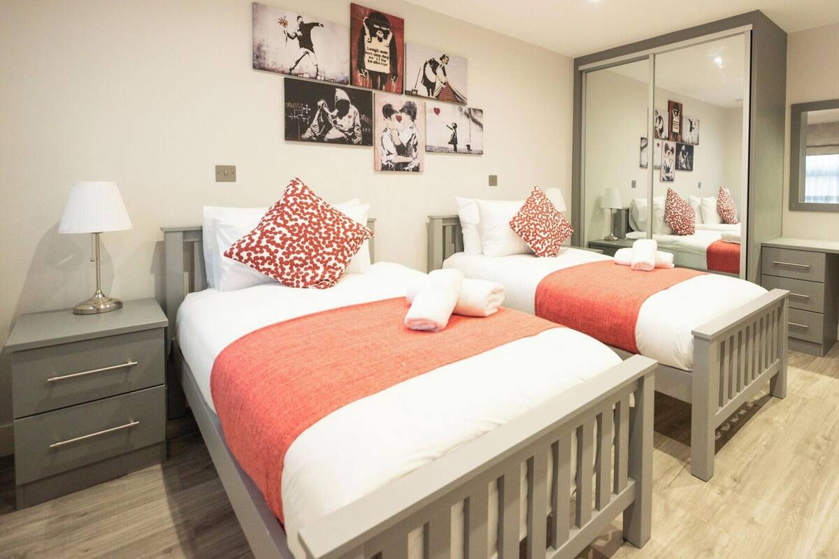 A hotel room with two beds, a desk, a chair, a mirror, and artwork on the walls.