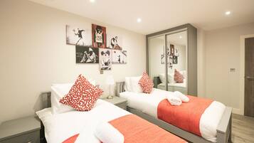 Habitación de hotel con dos camas, cada una con ropa de cama roja y blanca, una mesita de noche con lámpara y una pared decorada con cuadros enmarcados.