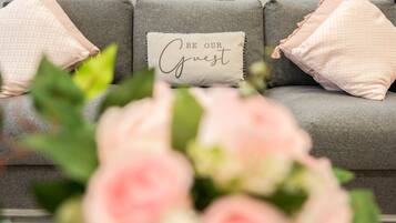 A grey sofa with three pillows, one with the text "BE OUR Guest".