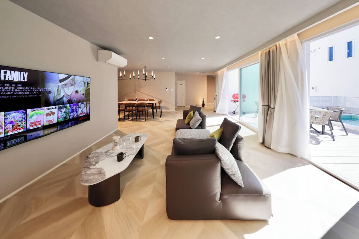 A modern living room with a flat-screen TV, a dining area, and a balcony with a pool.