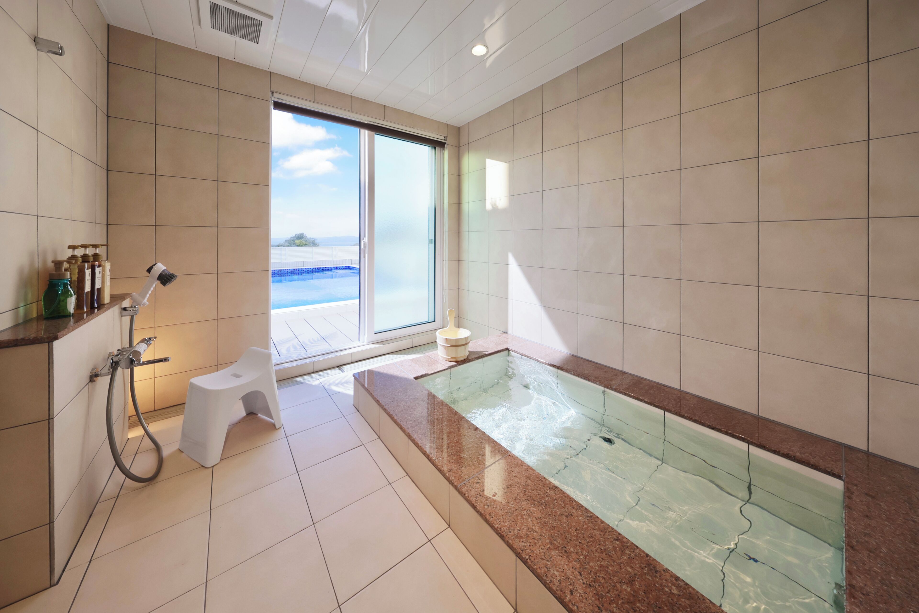 A modern bathroom with a glass-enclosed shower, a small stool, and a bathtub with a view of the sea.
