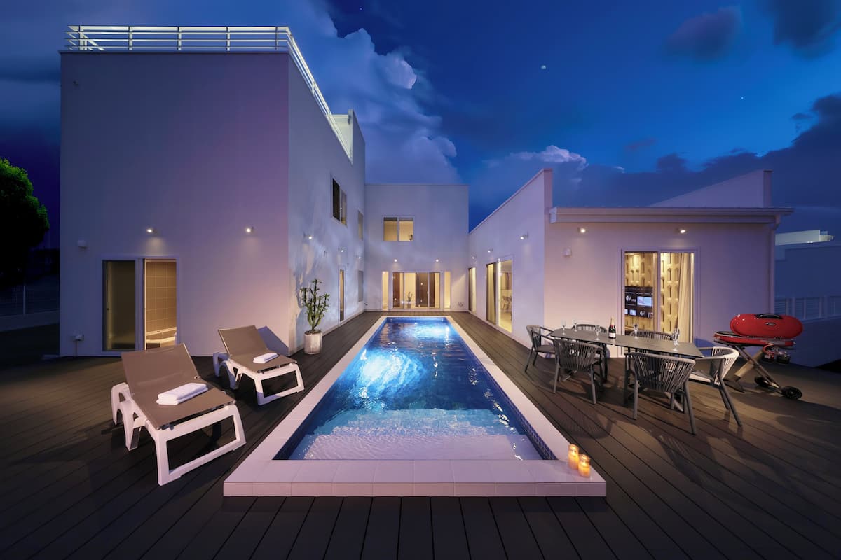 A modern outdoor pool area with lounge chairs, a barbecue setup, and a dining table.
