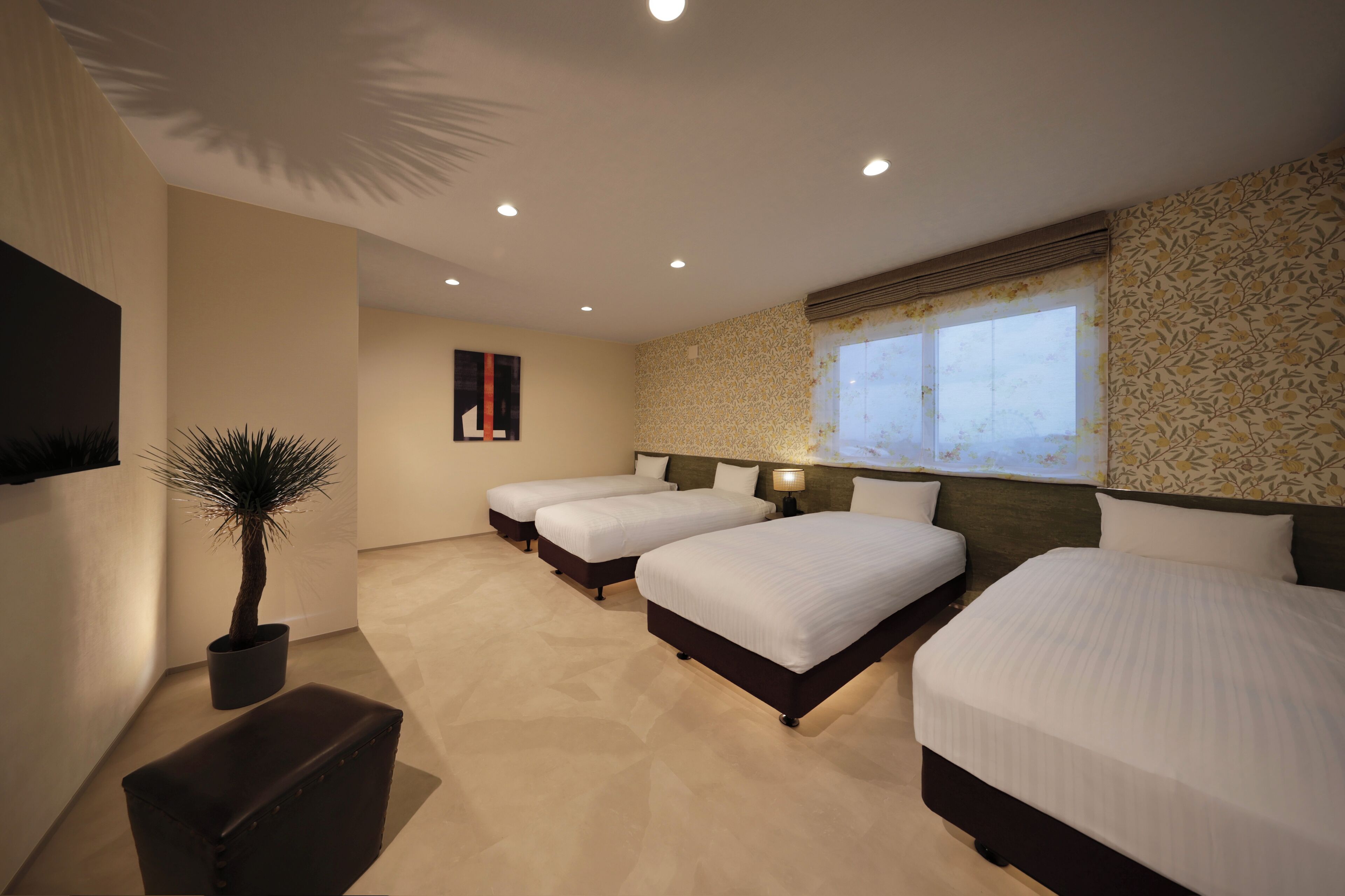 Ein Hotelzimmer mit drei Betten, einem Blumentopf, einer Bank und einem Fernseher an der Wand.