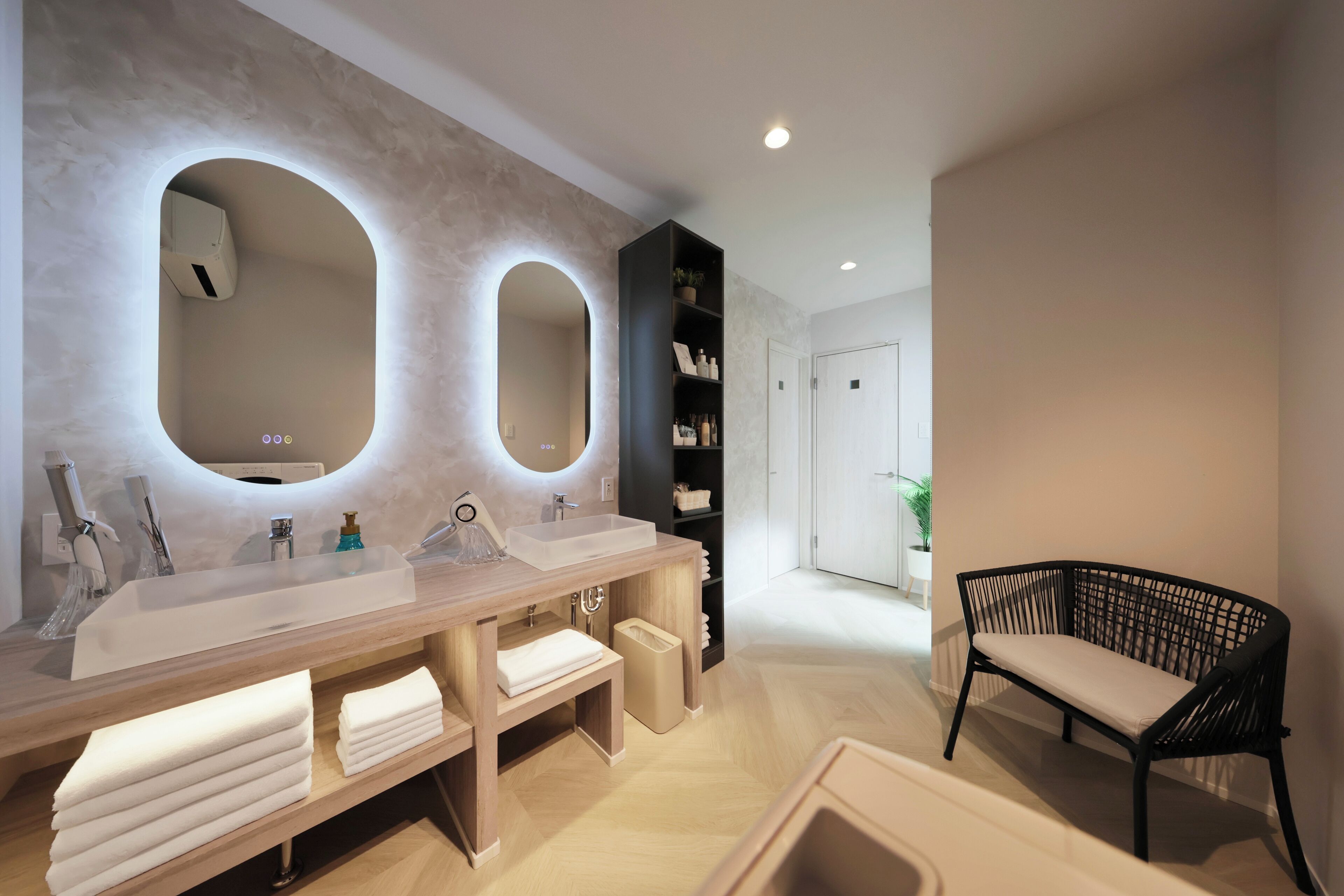 A modern bathroom with dual sinks, a large mirror, and a black wicker chair.