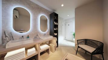 A modern bathroom with dual sinks, a large mirror, and a black wicker chair.