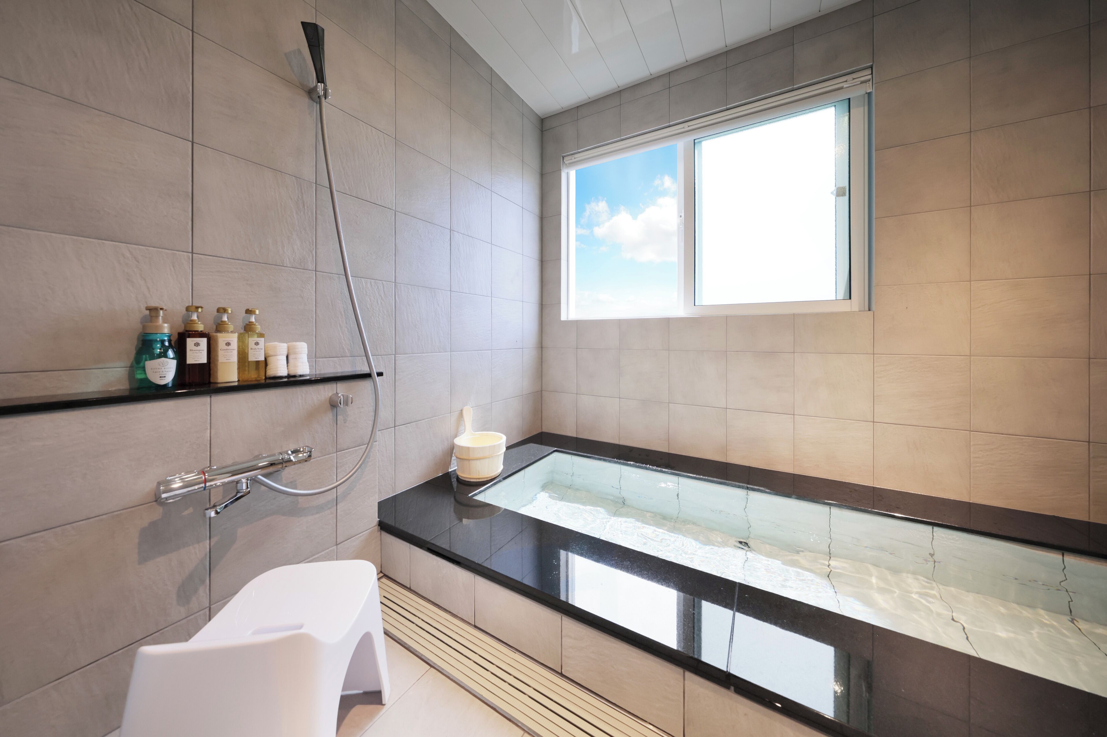 A modern bathroom with a glass-enclosed bathtub, a showerhead, and a shelf with toiletries.