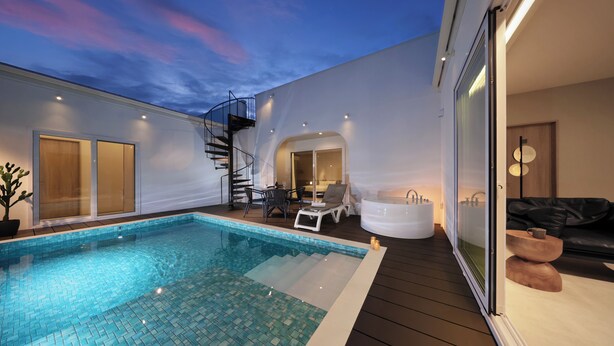 Uma área interna moderna com piscina, uma banheira de hidromassagem envidraçada, escadas e um espaço de estar com mesa e cadeiras.