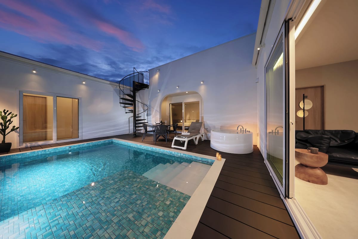 A modern indoor pool area with a glass-enclosed hot tub, a staircase, and a seating area with a table and chairs.