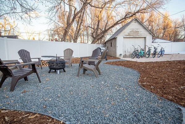A backyard with Adirondack chairs, a fire pit, and bicycles parked against a shed.