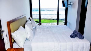 A bedroom with a bed, pillows, a rolled towel, and a view of the ocean through large windows. - Surfside Serenity Ahangama (Ahangama)