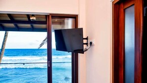 A room with a television mounted on the wall, a wooden door, and a view of the ocean through a glass door. - Surfside Serenity Ahangama (Ahangama)