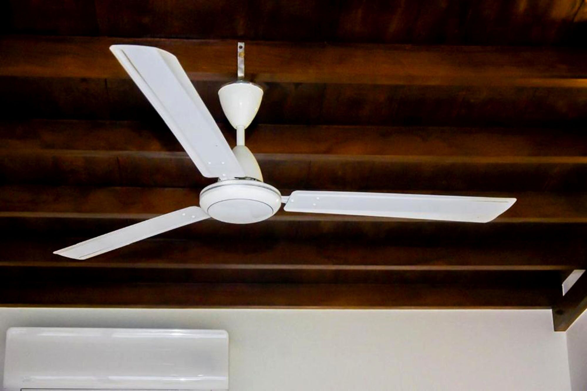 A ceiling fan with three blades and a central light fixture in a room with wooden paneling.