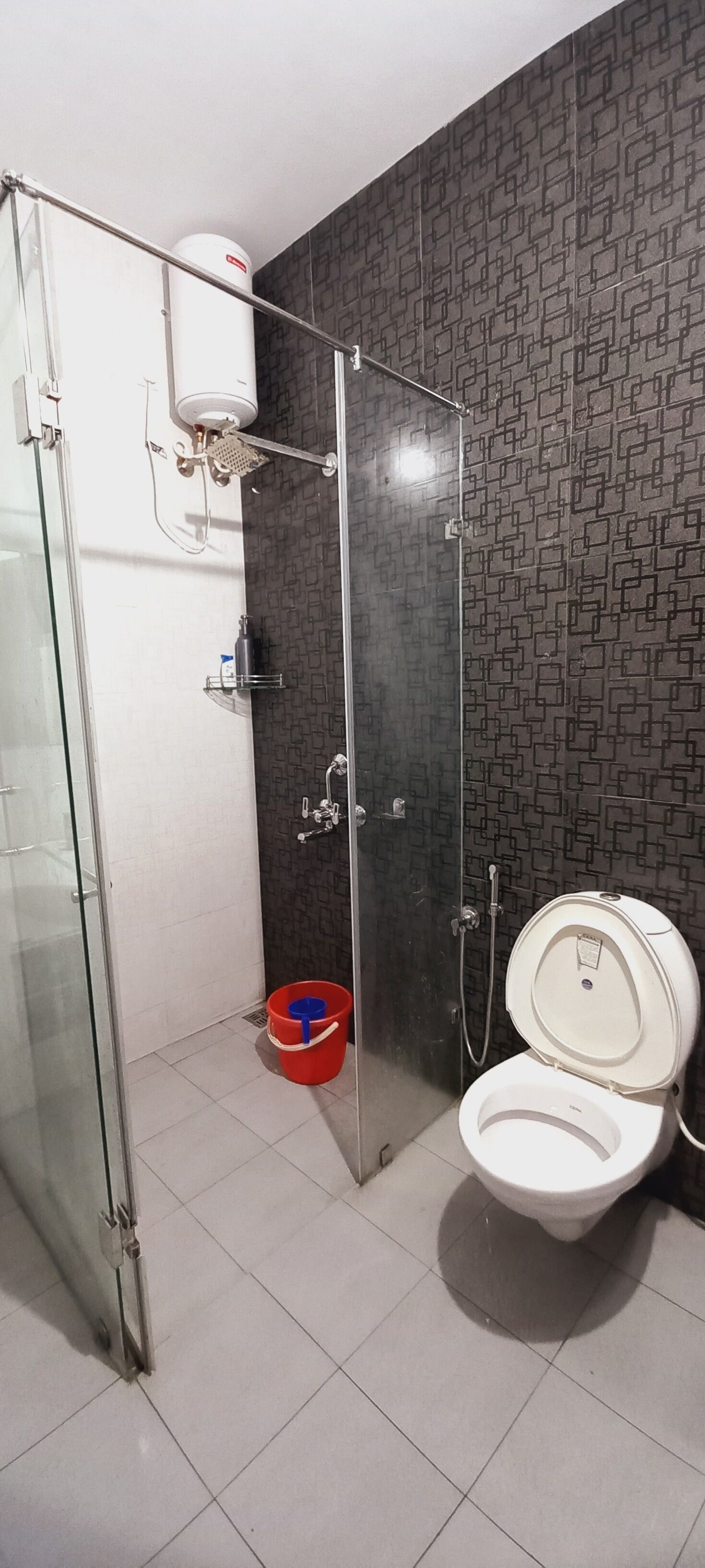 A bathroom with a glass shower enclosure, a toilet, and a red bucket on the floor.