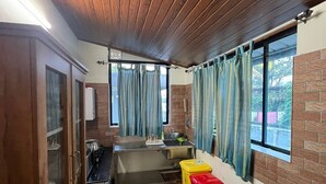 A compact kitchen with wooden ceiling, a sink, cabinets, and a window with curtains. - Two bedroom Villa overlooking Kzuhuppilly Beach (Kochi)