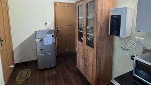 A compact kitchen with wooden cabinets, a refrigerator, a microwave, and a water dispenser. - Two bedroom Villa overlooking Kzuhuppilly Beach (Kochi)