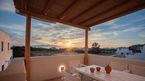 A terrace with a table and chairs, a view of the sunset, and a distant landscape.