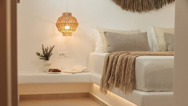 A modern bedroom with a white bed, a bedside table with a lamp, a small plant, and a book.