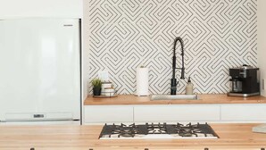 A modern kitchen with a central island, bar stools, a gas stove, a coffee machine, and a patterned backsplash. - Casa Serena, Oceanfront Lodging (El Sauzal)