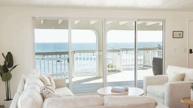 A spacious living room with a large sliding glass door leading to a balcony with a view of the ocean. - Casa Serena, Oceanfront Lodging (El Sauzal)
