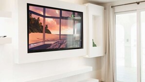 A flat-screen TV mounted on a white wall with a scenic beach view. - Casa Serena, Oceanfront Lodging (El Sauzal)