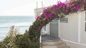 A coastal building with a staircase leading to a porch, surrounded by lush greenery and vibrant bougainvillea flowers. - Casa Serena, Oceanfront Lodging (El Sauzal)