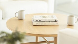 A cozy room with a round wooden table, two white mugs, and a stack of books titled 'ARAN' and 'HOMEBODY'. - Casa Serena, Oceanfront Lodging (El Sauzal)