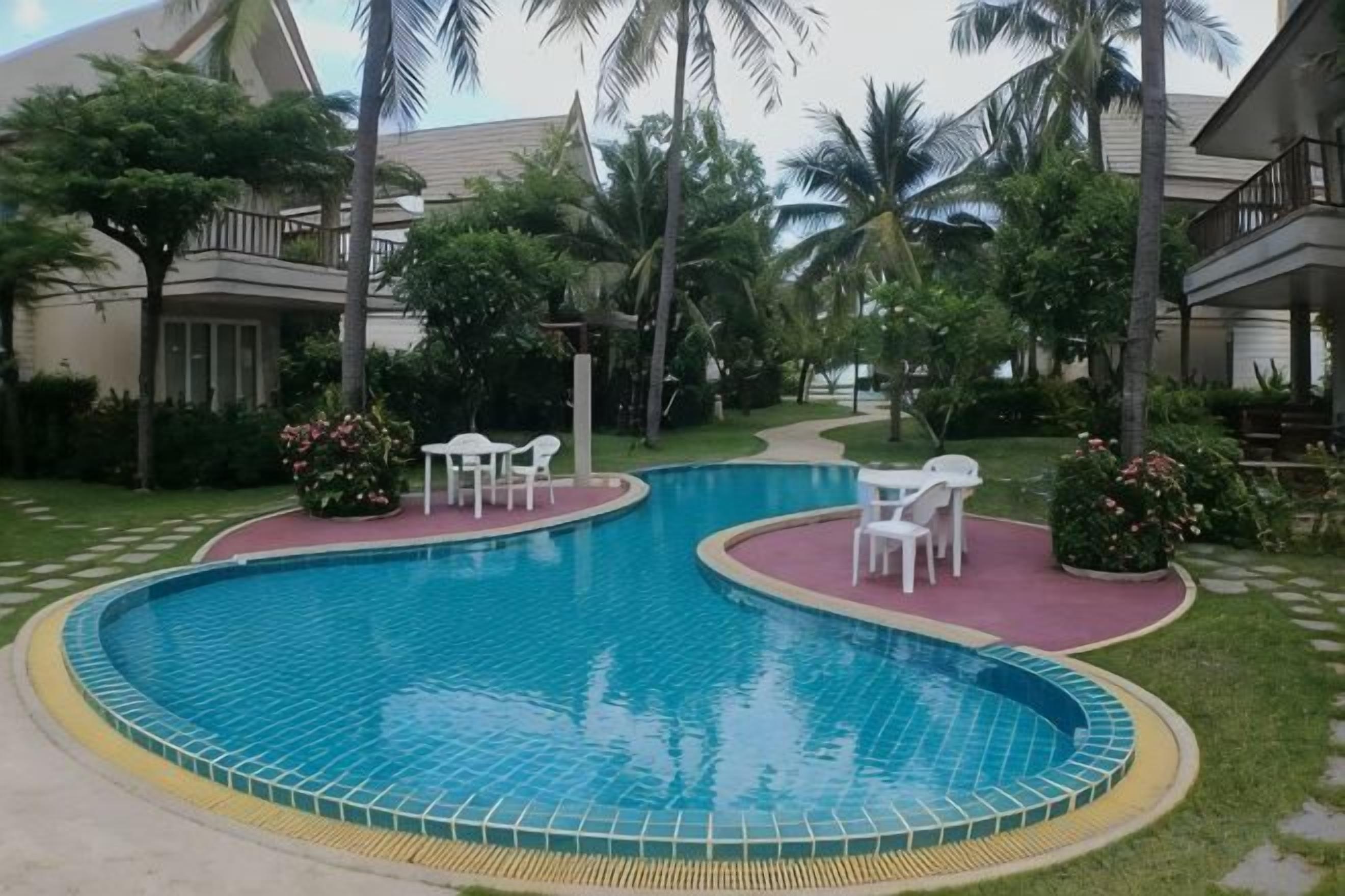 Ein Pool mit geschwungener Kante, umgeben von einer gepflasterten Fläche mit weißen Stühlen und Tischen.