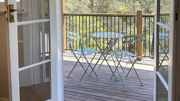 An open door to a wooden deck with a glass railing, a table, and chairs. - Rivendell House: Spacious retreat, pet friendly (Shadforth)