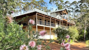 A two-story building with a balcony, surrounded by dense greenery and pink flowering plants. - Rivendell House: Spacious retreat, pet friendly (Shadforth)