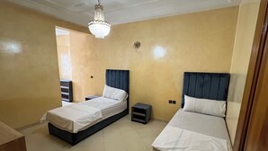 A small, well-lit bedroom with two single beds, a small bedside table, and a chandelier. - Almouahidine Residence (Fes)