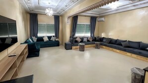A spacious living room with a large sectional sofa, a TV, and a wooden coffee table. - Almouahidine Residence (Fes)