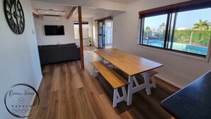 Ein modernes Wohnzimmer mit einem Holzespeisetisch, einem grauen Sofa, einem Flachbildfernseher und einem großen Fenster mit Blick auf einen Pool.