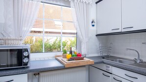 Une cuisine avec des meubles blancs, un évier, un four à micro-ondes et une fenêtre ornée de rideaux en dentelle.