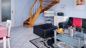 Un salon moderne avec un escalier en colimaçon en bois, un canapé en cuir noir, une table basse en verre et un coin repas avec une chaise et une table blanches.
