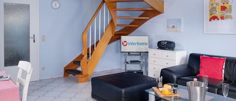 Una sala de estar moderna con una escalera espiral de madera, un sofá de cuero negro, una mesa de centro de vidrio y un comedor con una silla blanca y una mesa.