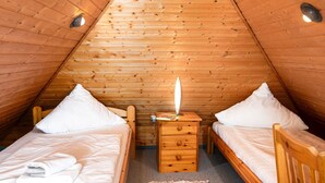 Une chambre mansardée chaleureuse, avec deux lits en bois, une table de chevet et un tapis rouge.