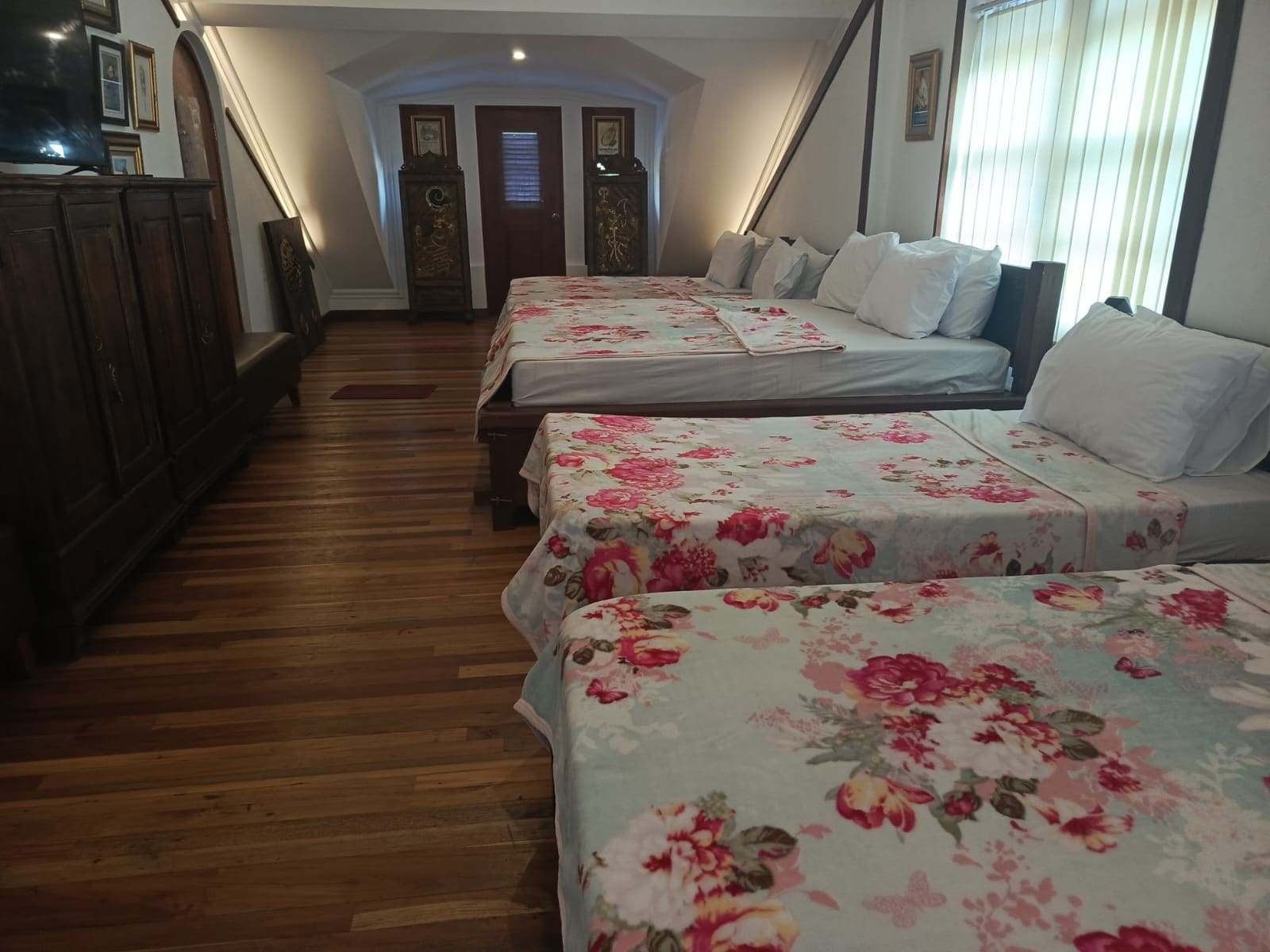 A hotel room with two beds, wooden flooring, and a hallway leading to a door.